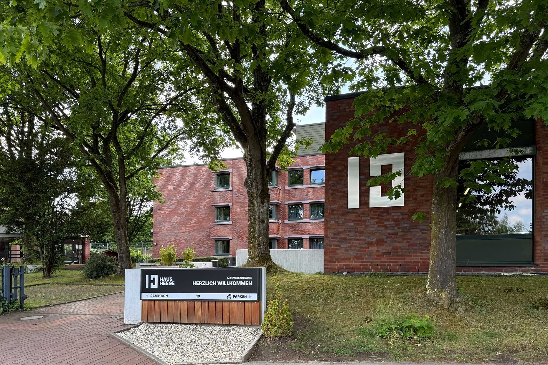 Auffahrt mit Willkommensschild und dem Hauptgebäude des Haus Heege
